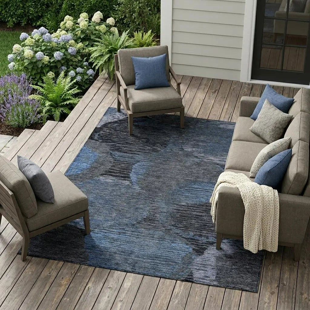 Gray and blue abstract area rug on a wooden patio, surrounded by plush seating and greenery.