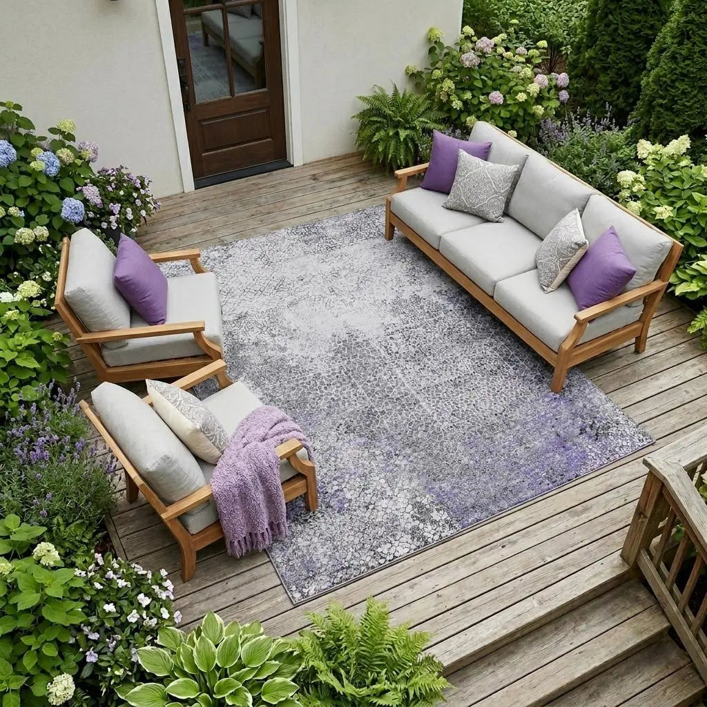 Elegant outdoor seating set with gray cushions and purple accents on a floral-patterned gray rug, surrounded by lush greenery.