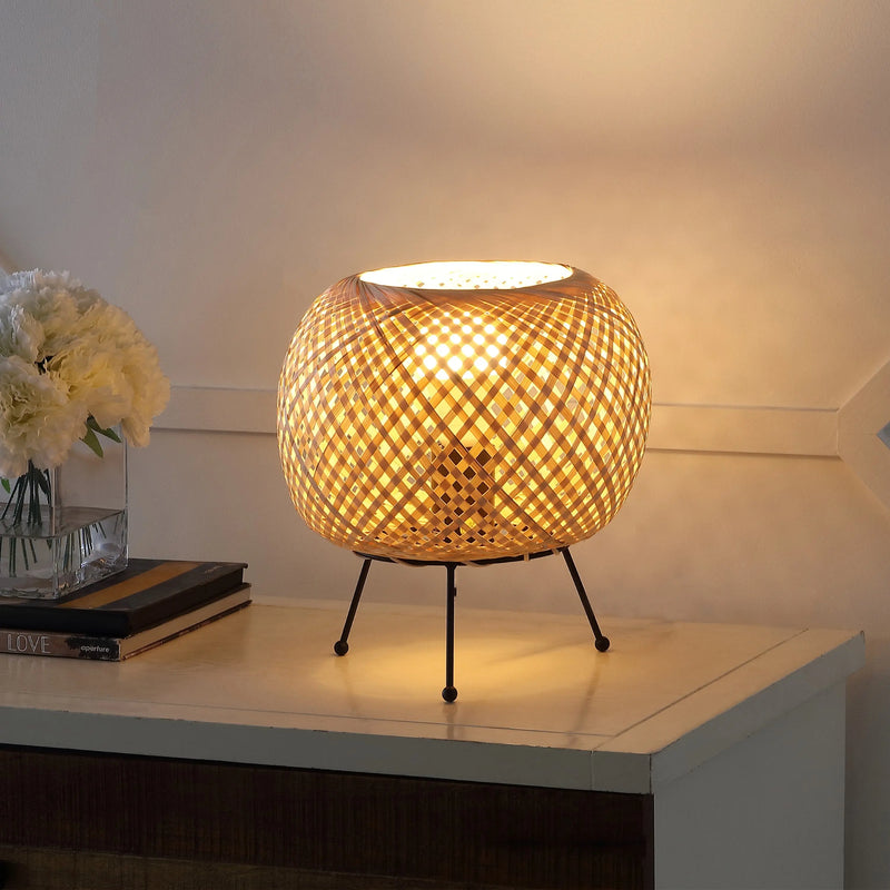 Woven rattan table lamp with a warm glow, featuring a black metal base and stylish, modern design. Perfect for ambient lighting.