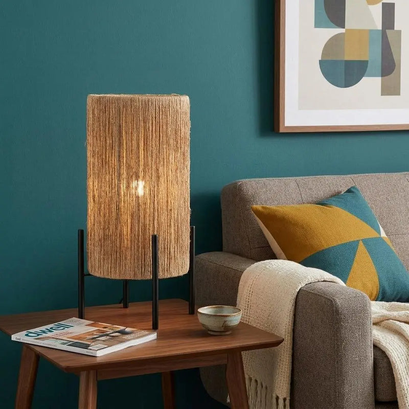 Natural woven lampshade table lamp with black metal stand, illuminating a cozy living room with teal walls and modern decor.