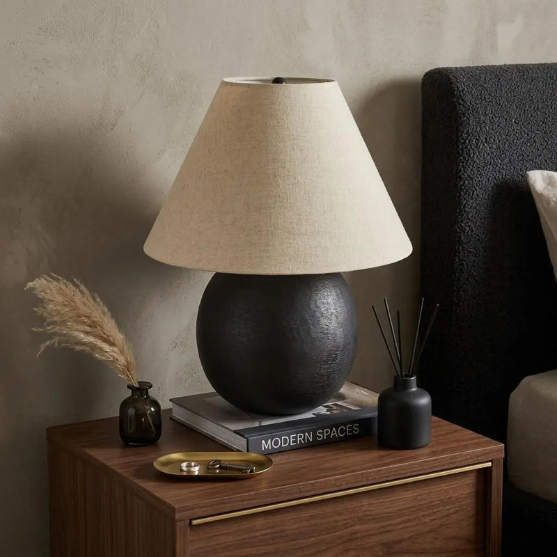 Black ceramic table lamp with beige linen shade, modern design on a wooden nightstand, enhancing contemporary decor.