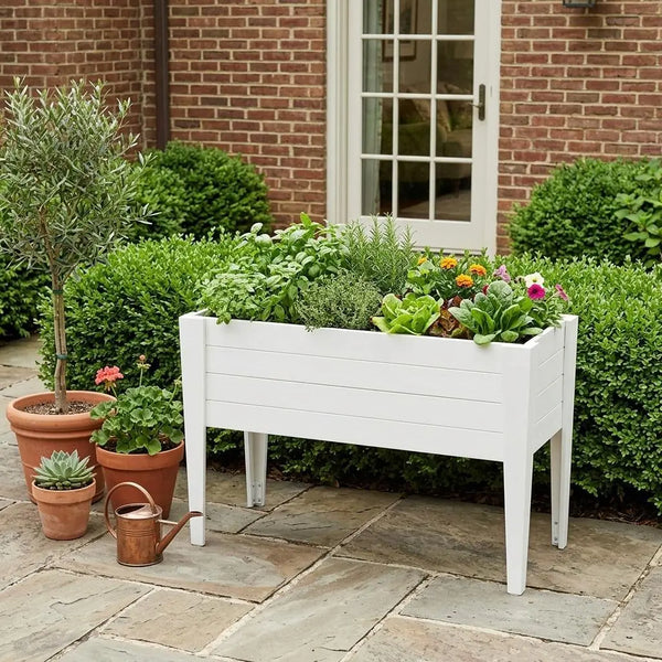 White wooden raised garden bed with colorful flowers, herbs, and greenery, set against a brick wall.