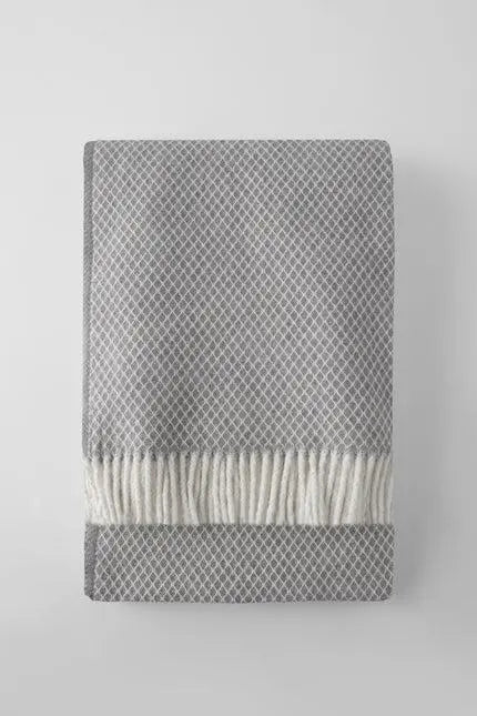 Gray patterned woven blanket with a soft cream fringe, perfect for cozying up in stylish comfort.
