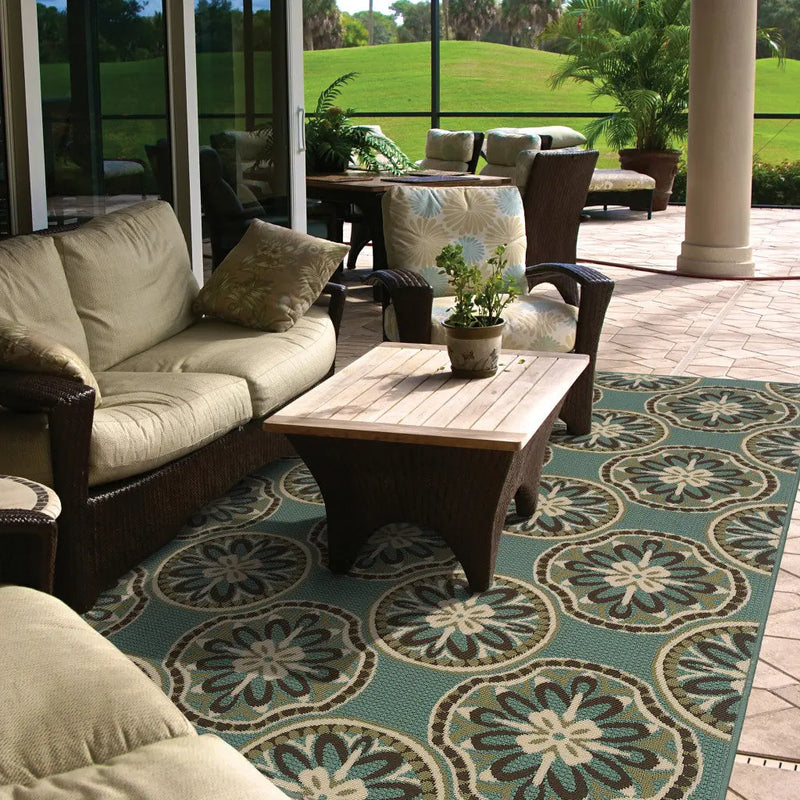 Outdoor patio rug in teal and beige, featuring floral patterns, paired with wicker furniture and a wooden coffee table.