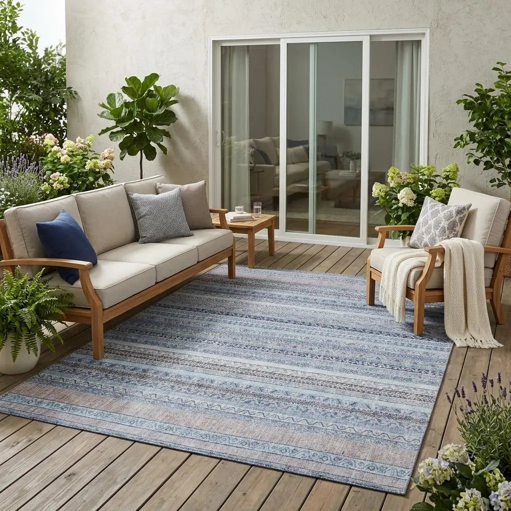 Light blue patterned outdoor rug on wooden patio, arranged with beige sofas and greenery. Perfect for stylish outdoor living.