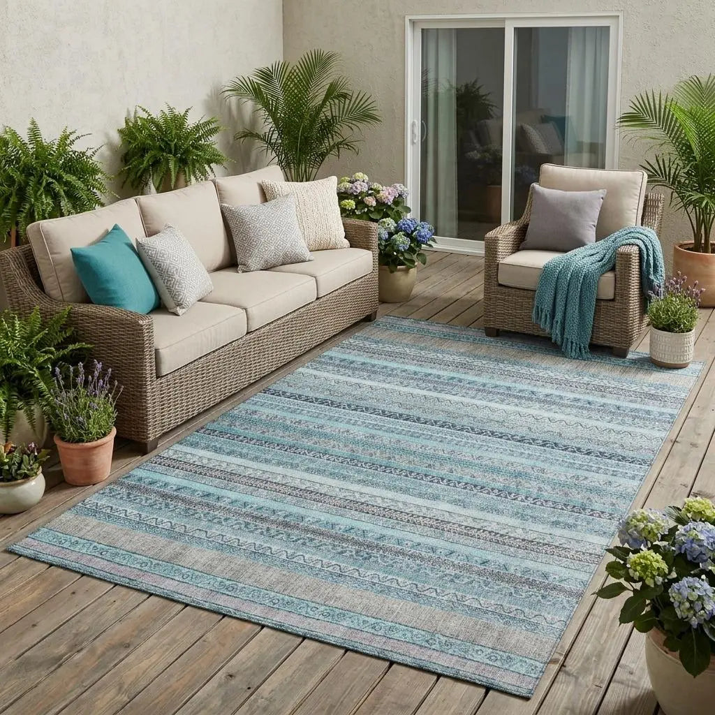 Blue and grey striped outdoor rug, woven texture, ideal for patios, complemented by beige wicker furniture and greenery.