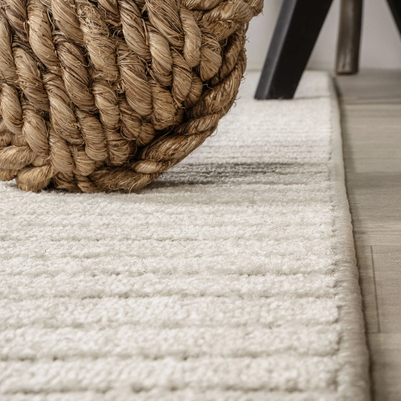 Natural jute storage basket in tan, placed on a soft cream textured area rug with a modern design.