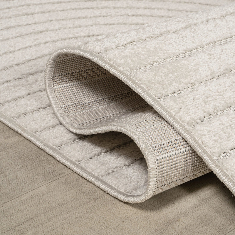 Beige plush area rug with a textured striped design, crafted from soft synthetic fibers on a light wood floor.