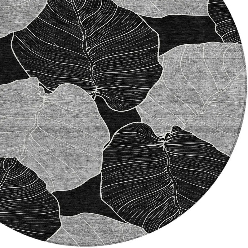 Round black and white area rug featuring abstract leaf designs in soft grey and white, perfect for modern decor.