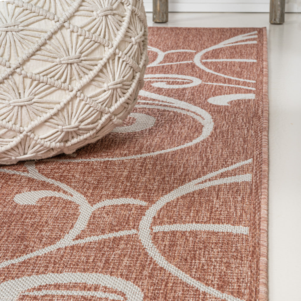 Terracotta woven area rug with white floral patterns, paired with a textured cream pouf, perfect for cozy home decor.