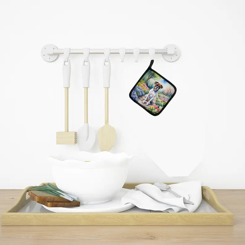 White ceramic bowl on a wooden tray with utensils, featuring a colorful dog-themed pot holder hanging nearby.