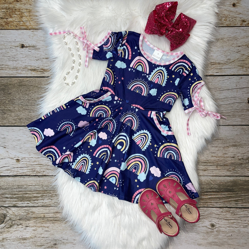 Navy rainbow print dress with pink accents, paired with pink shoes and bow, perfect for girls' casual wear.