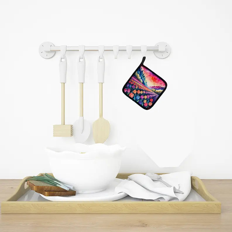 Colorful abstract print potholder, quilted fabric, hanging by white kitchen utensils in a vibrant, stylish kitchen setting.