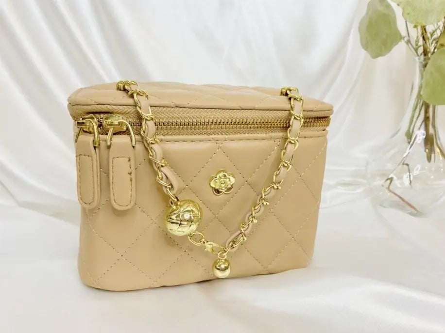 Beige quilted cosmetic bag with gold chain and charm, perfect for stylish organization.