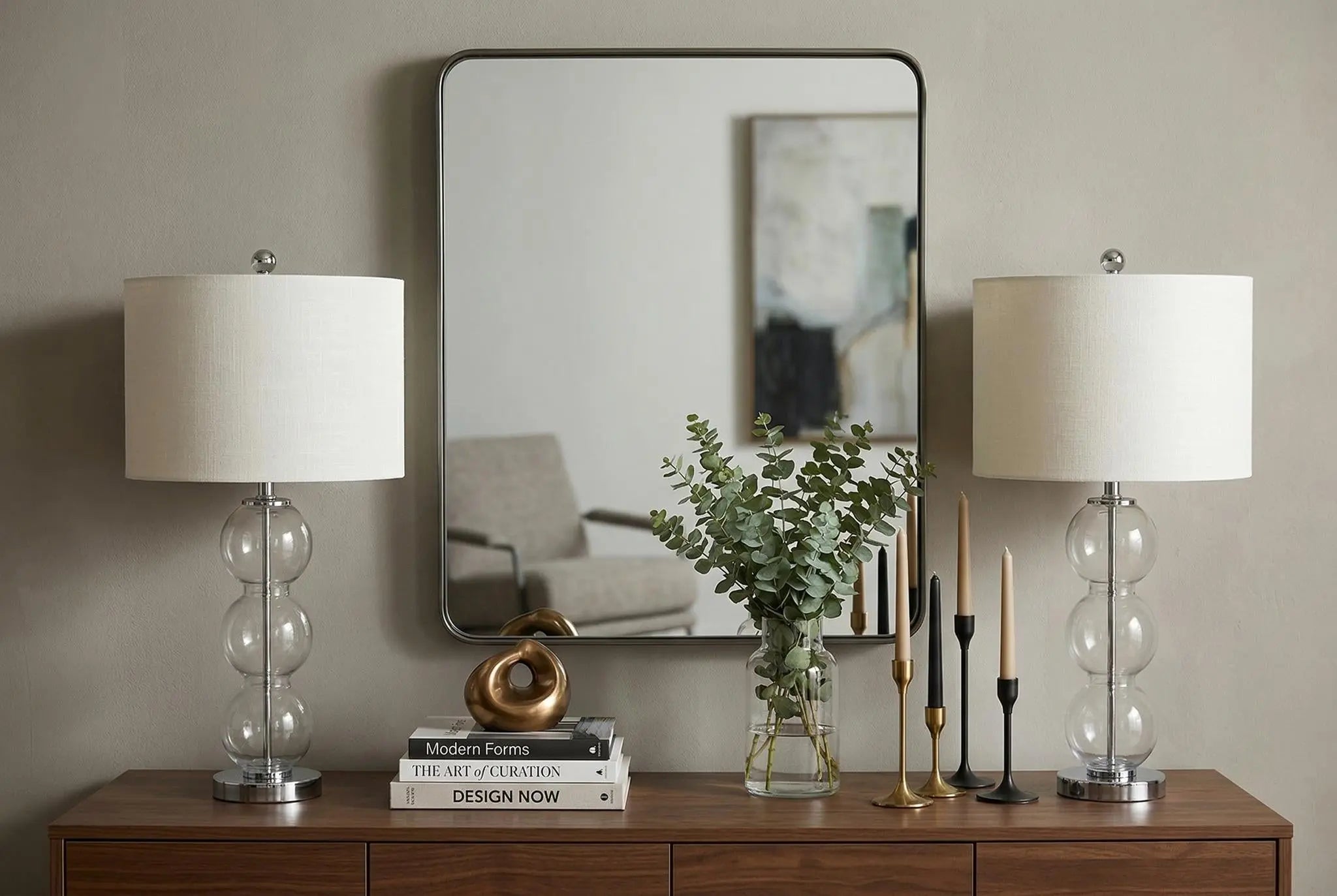 Elegant glass table lamps with white linen shades, a modern mirror, and decorative elements on a wood console table.