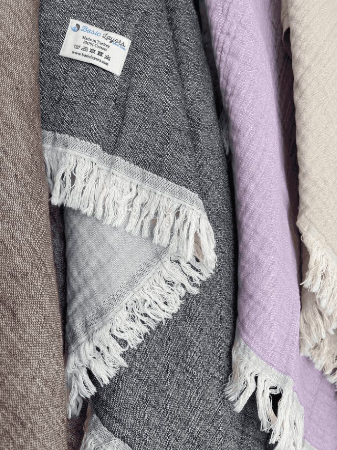 Cozy woven blankets in grey, lavender, and taupe with fringe edges, perfect for stylish home decor or gifting.